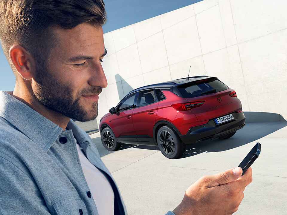 Чоловік дивиться на екран смартфона біля Opel Grandland